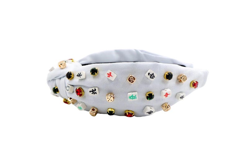 A white headband with a twisted design, adorned with various colorful gemstone studs and Mahjong tile charms, conveying a playful and eclectic style.