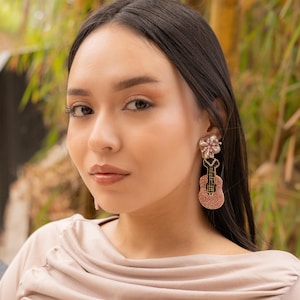 Close-up of a woman showcasing elegant guitar-shaped earrings in a natural setting.