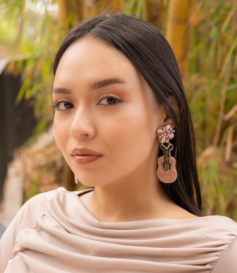 Close-up of a woman showcasing elegant guitar-shaped earrings in a natural setting.