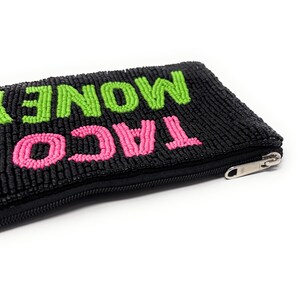 May include: Black beaded pouch with the words "TACO MONEY" in bright pink and green beads. The pouch has a black zipper and is likely used for carrying small items like cash or cards. The design is fun and playful.