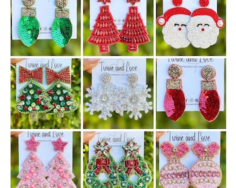 May include: A collection of beaded Christmas earrings in various designs. Styles include Christmas trees, Santa faces, snowflakes, and ornaments. Colors include red, green, pink, and white. Each pair is attached to a white card with the text "Twine and Love".