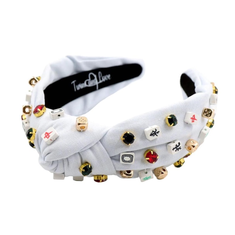 A white headband with a twisted design, adorned with various colorful gemstone studs and Mahjong tile charms, conveying a playful and eclectic style.
