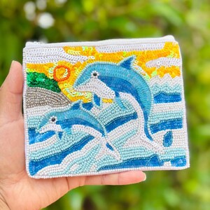 This beautifully hand-beaded Dolphins Beaded Pouch Purse features intricate seed beads and sparkling sequins, highlighted by two charming dolphins. Its compact size makes it an elegant and practical accessory, perfect for carrying your essentials with a touch of unique artistry.