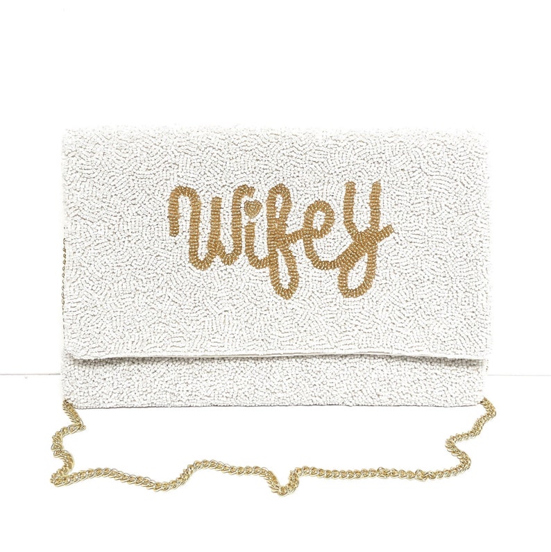 Op de afbeelding: Witte parelclutch met een gouden kettingband en het woord "wifey" in gouden parels.