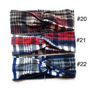 May include: Three plaid fabric headbands in different colour combinations. The top headband is black, brown, and red plaid. The middle headband is red, white, and blue plaid. The bottom headband is grey, white, and blue plaid. Each headband has a number tag attached to it: #20, #21, and #22.