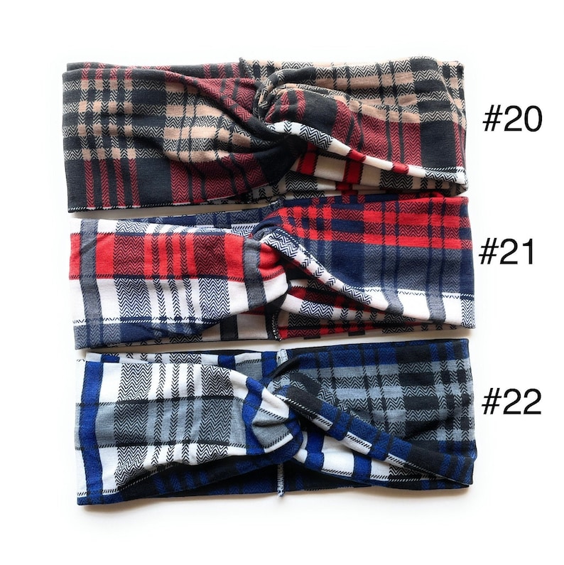May include: Three plaid fabric headbands in different colour combinations. The top headband is black, brown, and red plaid. The middle headband is red, white, and blue plaid. The bottom headband is grey, white, and blue plaid. Each headband has a number tag attached to it: #20, #21, and #22.