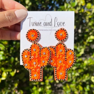May include: Orange and black beaded cactus earrings with rhinestones. The earrings are on a white card with the text "Twine and Love" and "twineandlove.com".