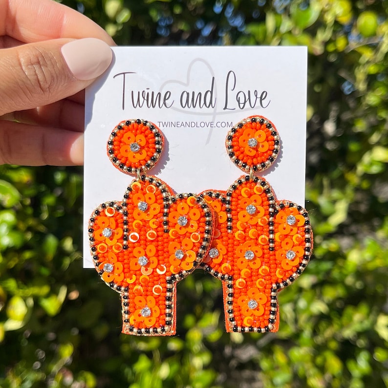 May include: Orange and black beaded cactus earrings with rhinestones. The earrings are on a white card with the text "Twine and Love" and "twineandlove.com".