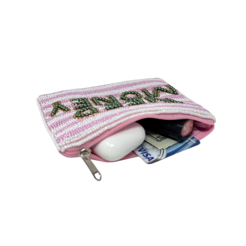May include: A pink and white beaded pouch with the word "MONEY" in green beads. The pouch is open, revealing a white earbud, lipstick, cash, and a credit card. The zipper is silver.