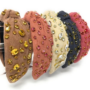 May include: Five fabric headbands with a knotted design and embellished with rhinestones. The headbands are in various colors, including brown, pink, beige, gray, and red.
