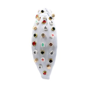 A white headband with a twisted design, adorned with various colorful gemstone studs and Mahjong tile charms, conveying a playful and eclectic style.