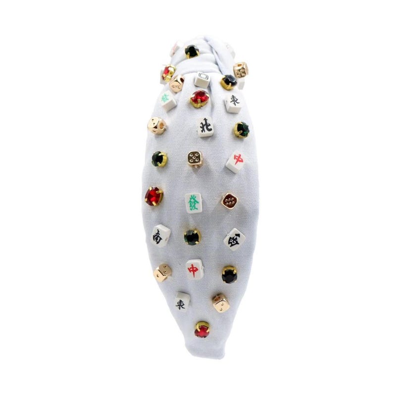 A white headband with a twisted design, adorned with various colorful gemstone studs and Mahjong tile charms, conveying a playful and eclectic style.
