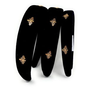 May include: Black velvet headbands with gold-colored bee embellishments. The headbands are thick and have a soft, plush texture. The bees are intricately detailed and add a touch of elegance to the hair accessories.