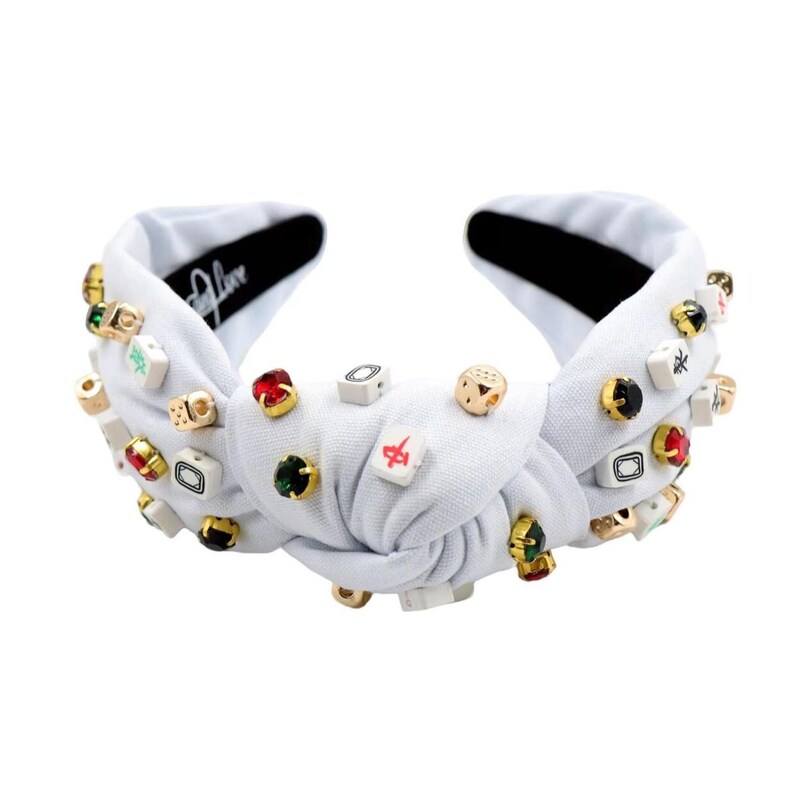 A white headband with a twisted design, adorned with various colorful gemstone studs and Mahjong tile charms, conveying a playful and eclectic style.