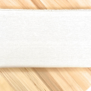 May include: A plain white clutch purse with a beaded trim. The clutch is made of a textured fabric and has a rectangular shape.