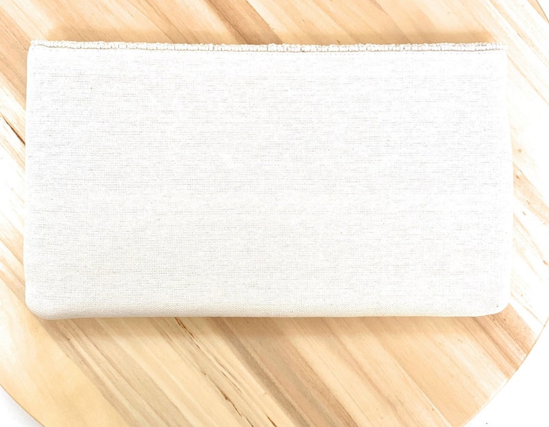 May include: A plain white clutch purse with a beaded trim. The clutch is made of a textured fabric and has a rectangular shape.