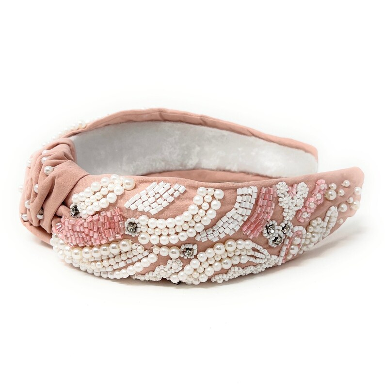 May include: A pink headband with a knotted design and embellished with white and pink beads.