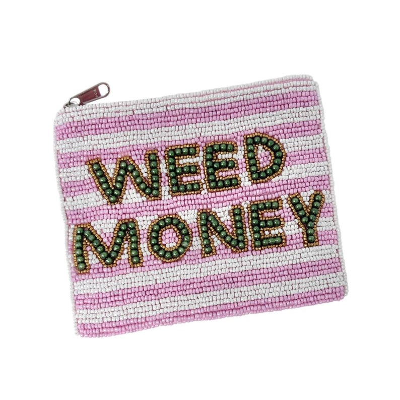 May include: A beaded coin purse with a pink and white striped pattern. The words "WEED MONEY" are spelled out in green beads. The purse has a small zipper with a brown pull.