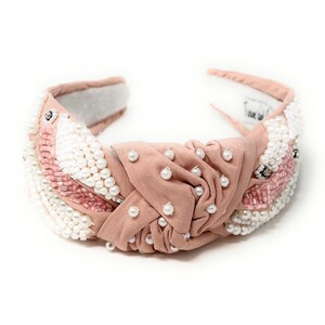 May include: A blush pink headband with a knotted design and pearl and pink bead embellishments.