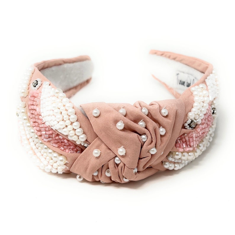 May include: A blush pink headband with a knotted design and pearl and pink bead embellishments.