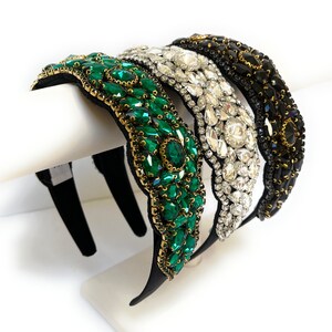 May include: Three headbands with different colored jeweled embellishments. The headband on the left has emerald green jewels, the middle headband has clear jewels, and the headband on the right has black jewels.