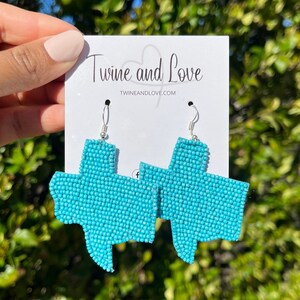May include: Turquoise blue beaded Texas state earrings with silver hooks. The earrings are displayed on a white card with the text "Twine and Love" and the website "twineandlove.com".