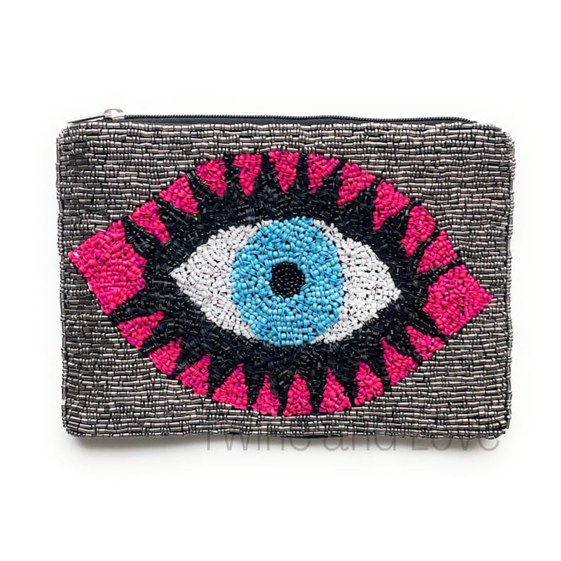 May include: A beaded clutch bag with a large, colorful evil eye design. The eye is blue, white, and black with pink accents. The bag is made of silver beads.