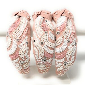 May include: Three pink fabric headbands with a knotted design. Each headband is decorated with white and pink pearls and beads in a floral pattern.