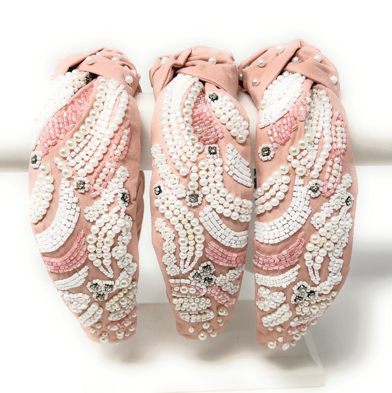 May include: Three pink fabric headbands with a knotted design. Each headband is decorated with white and pink pearls and beads in a floral pattern.