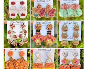 Op de afbeelding: Een verzameling kralen oorbellen met herfstthema's. Ontwerpen omvatten pompoenen, esdoornbladeren, koffiekopjes, kalkoenen, eikels, snoepmaïs en vossen. Elk paar oorbellen wordt gepresenteerd op een witte kaart met de tekst "Twine and Love".