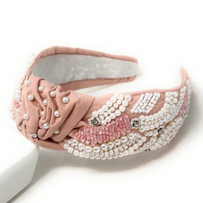 May include: A pink knotted headband with white and pink pearl and bead embellishments.