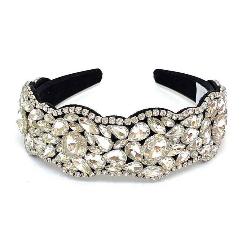 May include: A black headband with a wide band of clear rhinestones. The rhinestones are arranged in a wavy pattern and are of various sizes.