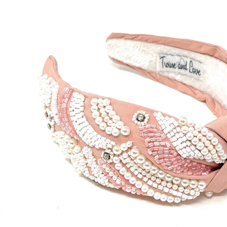 May include: A pink knotted headband with a pearl and pink bead design. The headband has a white fabric lining and the text "Trove and Love" is printed on the back.