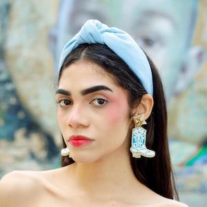 Statement cowboy boot earrings with turquoise accents worn by a model, creating a fun blend of western charm and modern fashion.