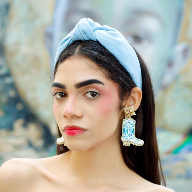 Statement cowboy boot earrings with turquoise accents worn by a model, creating a fun blend of western charm and modern fashion.