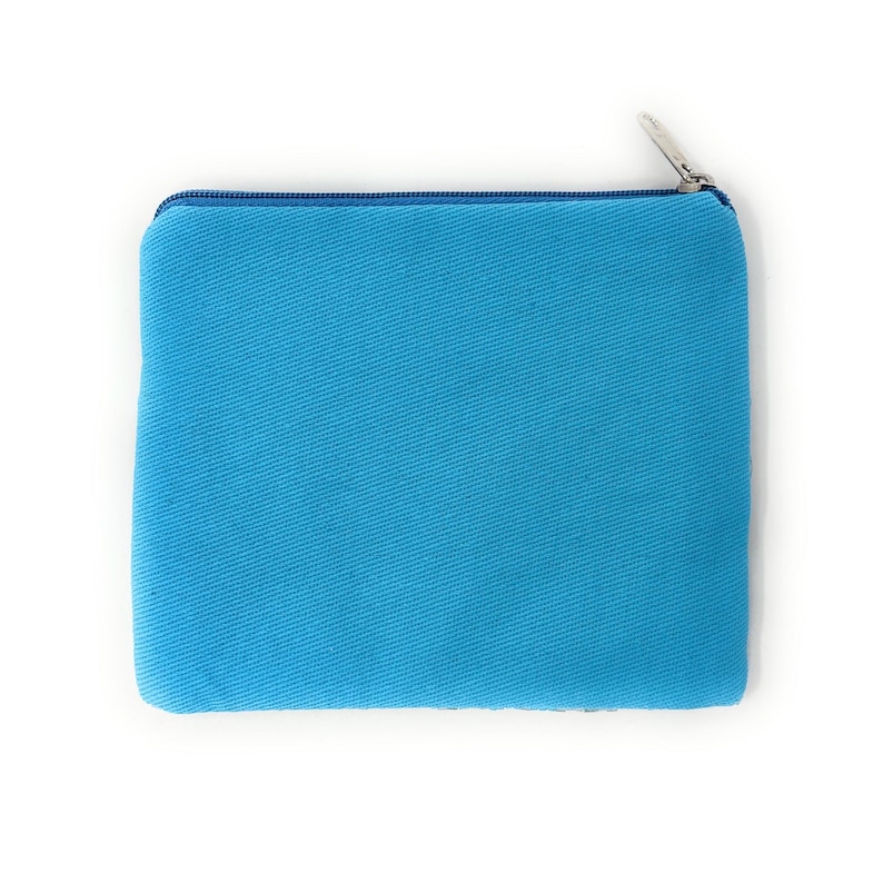 K&ouml;nnte beinhalten: Eine quadratische, t&uuml;rkisfarbene Rei&szlig;verschlusstasche. Die Tasche hat einen blauen Rei&szlig;verschluss und einen silbernen Metall-Rei&szlig;verschlussanh&auml;nger. Der Stoff hat ein subtiles, strukturiertes Aussehen. Die Tasche wird wahrscheinlich zur Aufbewahrung kleiner Gegenst&auml;nde verwendet.