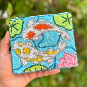 Elevate your accessory collection with our stunning Koi Beaded Pouch Purse. Meticulously hand-beaded with shimmering sequins and intricate beadwork, this eye-catching purse captures attention while maintaining the perfect size for your essentials. The beautiful craftsmanship makes this an irresistible statement piece you won't want to pass up.