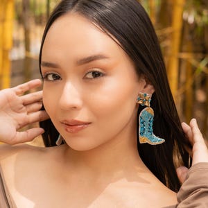 model showcasing colorful boot-shaped earrings in a natural setting.