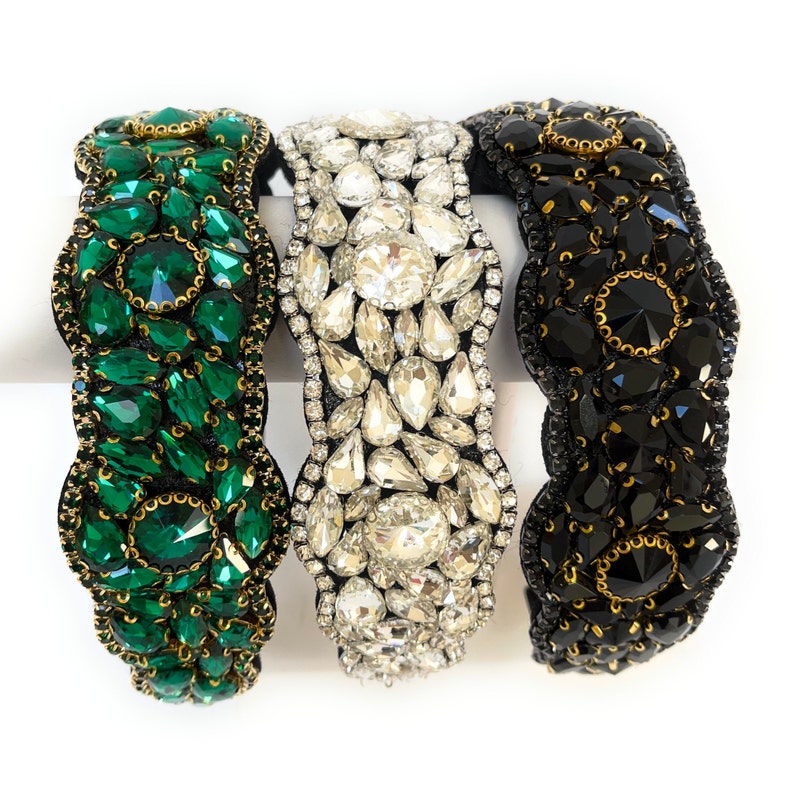 May include: Three headbands with different colored rhinestones. The headband on the left has green rhinestones, the middle headband has clear rhinestones, and the headband on the right has black rhinestones.