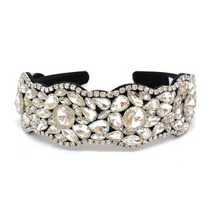 May include: A black headband with a row of large, clear rhinestones. The rhinestones are arranged in a wavy pattern and are set in a black fabric base.