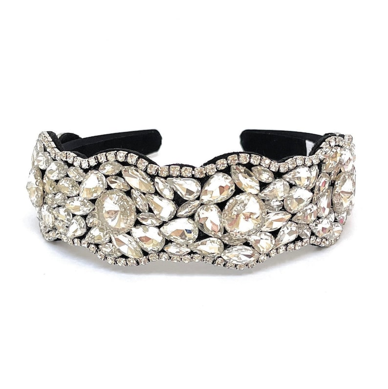 May include: A black headband with a row of large, clear rhinestones. The rhinestones are arranged in a wavy pattern and are set in a black fabric base.