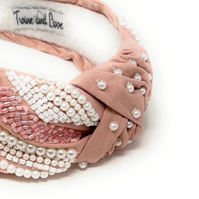 May include: A blush pink knotted headband with a pearl and beaded embellishment. The headband has the text "Twine and Love" on the back.