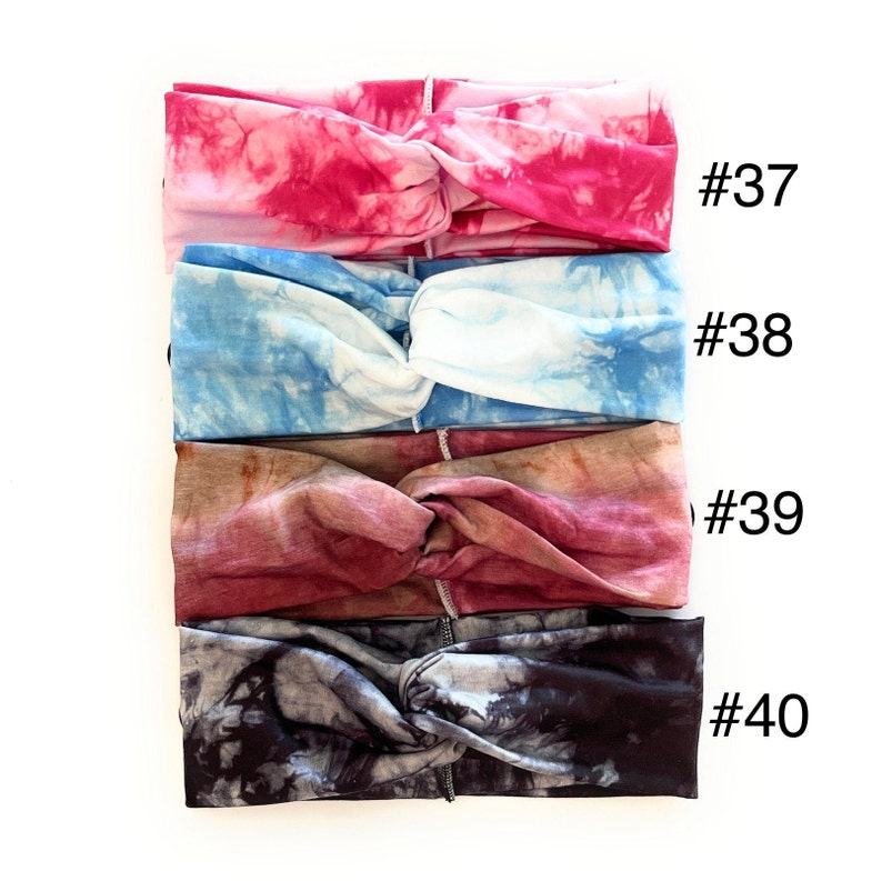 May include: Four tie-dye headbands in different colours: pink, blue, burgundy, and grey. The headbands are all knotted in the centre and have a tie-dye pattern. The numbers #37, #38, #39, and #40 are written next to each headband.