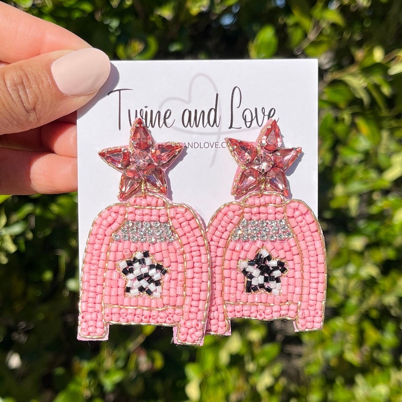 May include: Pink beaded earrings with a star charm and a checkerboard star design. The earrings are on a white card with the text "Twine and Love".
