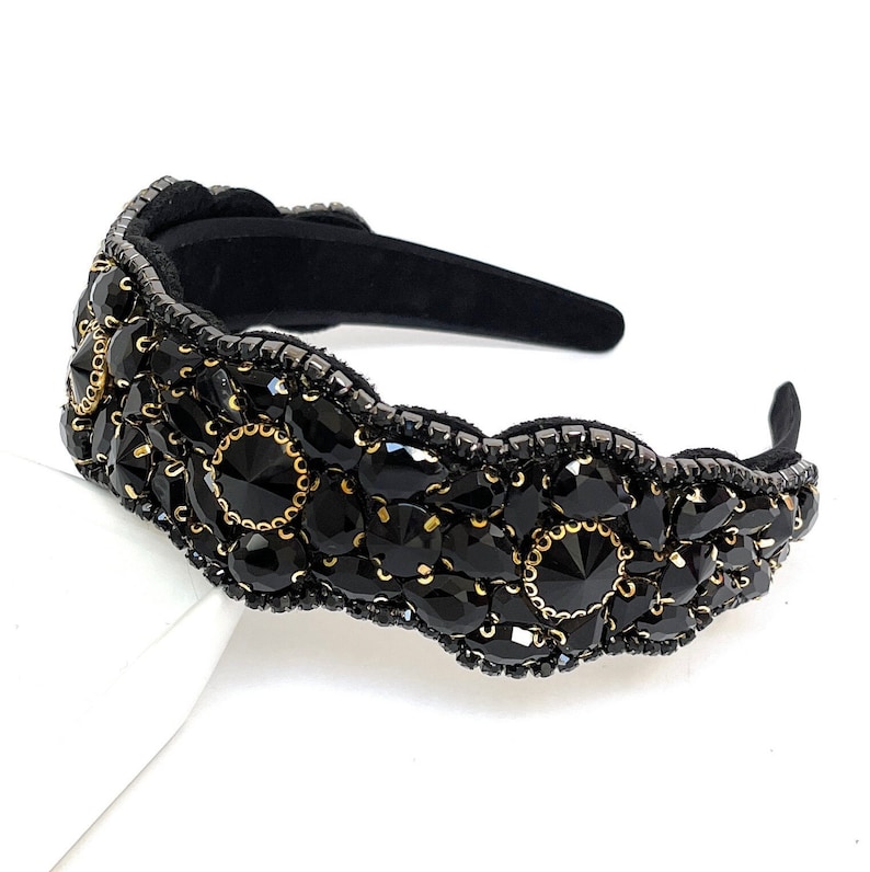 May include: Black headband with a decorative design of black and gold rhinestones.