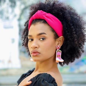 Western-inspired statement earrings shaped like pink cowgirl boots with sparkling embellishments and jeweled floral tops.