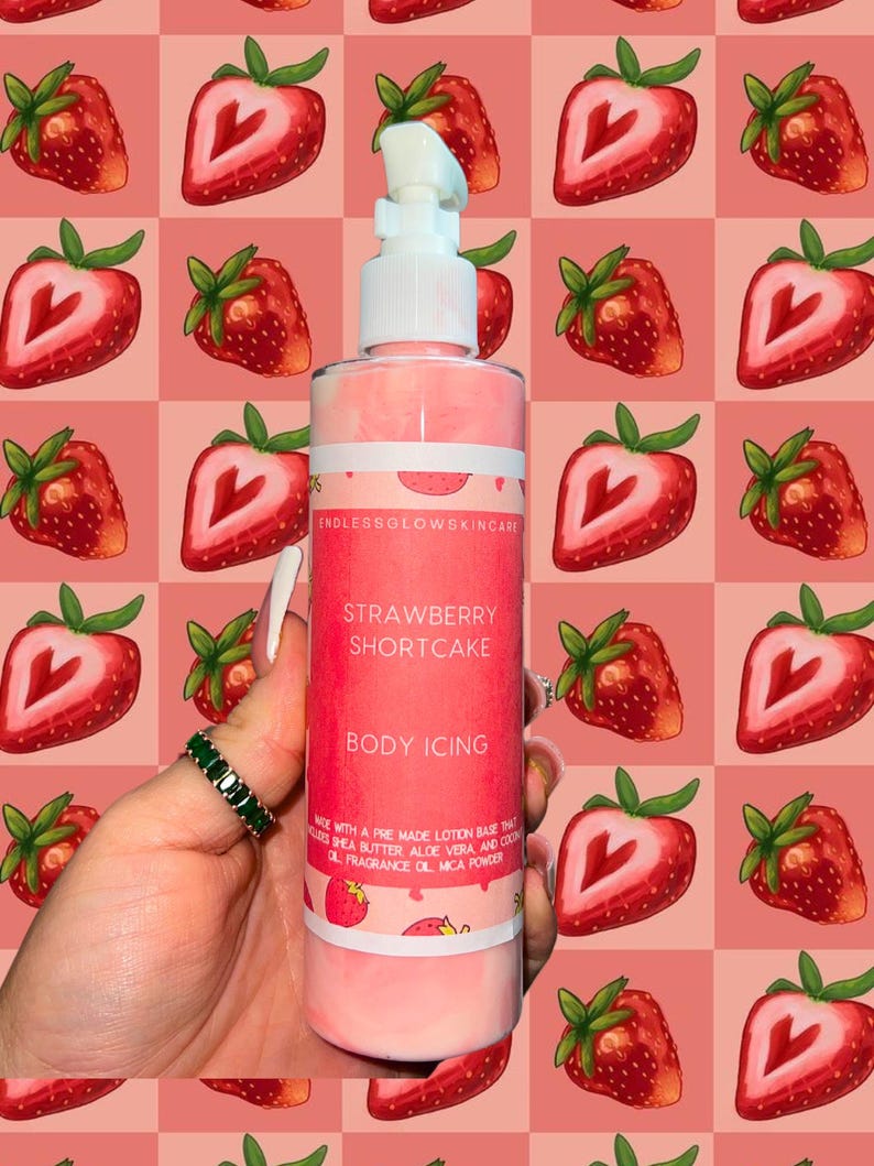 May include: A pink body lotion bottle with a white pump, labeled "Strawberry Shortcake Body Icing." The bottle is held against a pink and red strawberry pattern background. The label includes the brand name "Endless Glow Skincare."