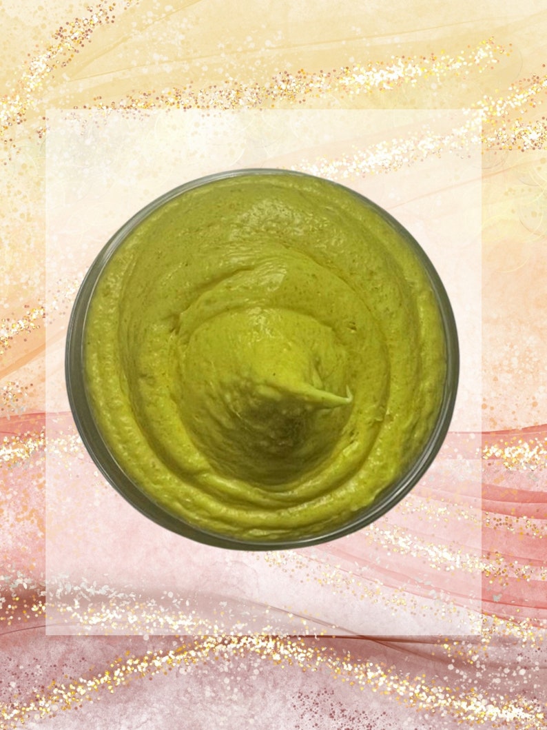 May include: A jar filled with a light green, creamy substance. The product has a smooth, textured appearance. The jar is clear, and the background has a watercolor effect with pink, gold, and white tones. The product appears to be a cosmetic or skincare item.