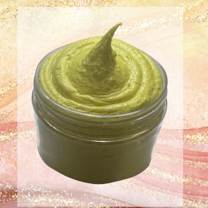 May include: A jar of light green, creamy product with a swirl design and a pointed top. The clear jar sits against a soft, abstract background with gold glitter accents. The product appears to be a skincare item.