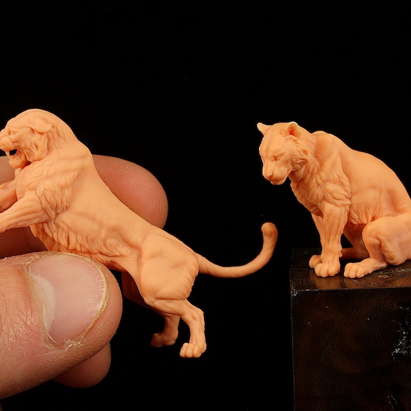 May include: Two detailed, hand-painted, miniature figurines of lions, one standing and one sitting, both in a light peach color.